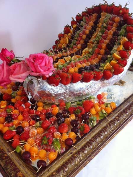 Plateau de brochettes de fruits variés disposées artistiquement autour d'une structure décorée de roses.