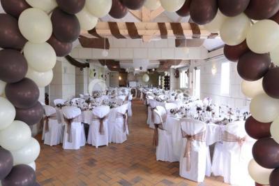 Salle avec des rangées de chaises en plastique blanc disposées face à une scène lumineuse dans un espace aux murs clairs.