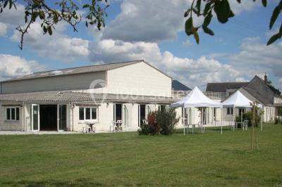 Salle avec des rangées de chaises en plastique blanc disposées face à une scène lumineuse dans un espace aux murs clairs.