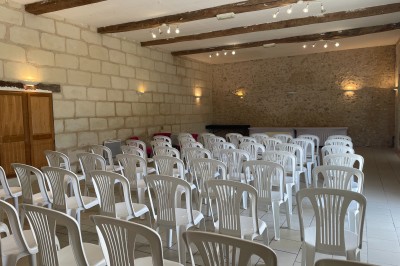 Miniature Traiteur Azay-le-Rideau (Indre-et-Loire) - Rousseau Traiteur #12 Salle avec des rangées de chaises en plastique blanc disposées face à une scène lumineuse dans un espace aux murs clairs.
