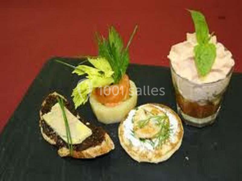Assortiment d'amuse-bouches comprenant tartines, verrine, blinis et garnitures variées sur une assiette noire.