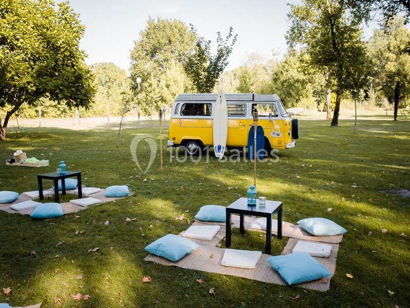Un van jaune stationné dans un parc verdoyant, entouré de coussins et de tables basses pour un pique-nique.