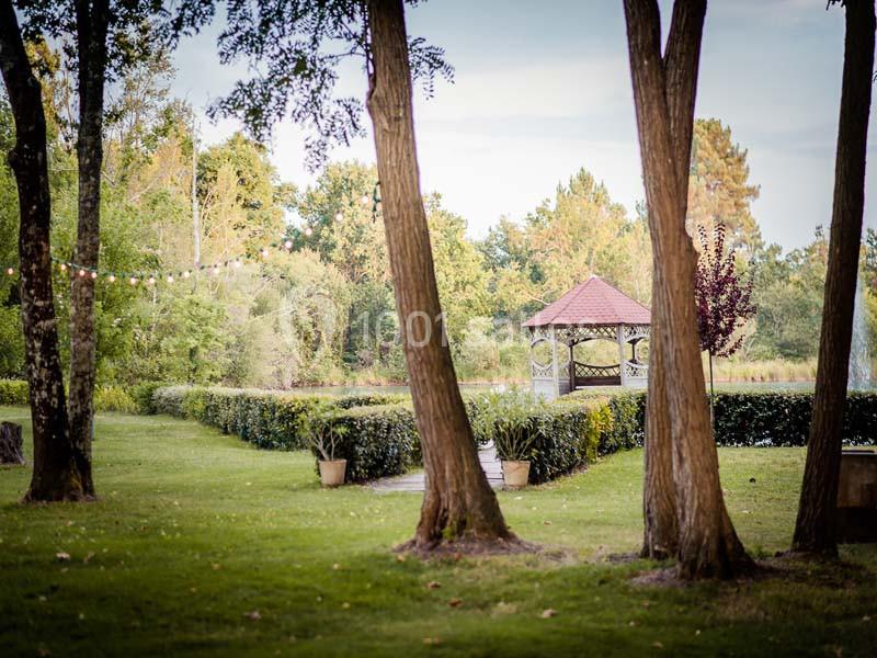 Kiosque en bois avec toit rouge entouré de verdure, arbres au premier plan et guirlandes lumineuses suspendues.