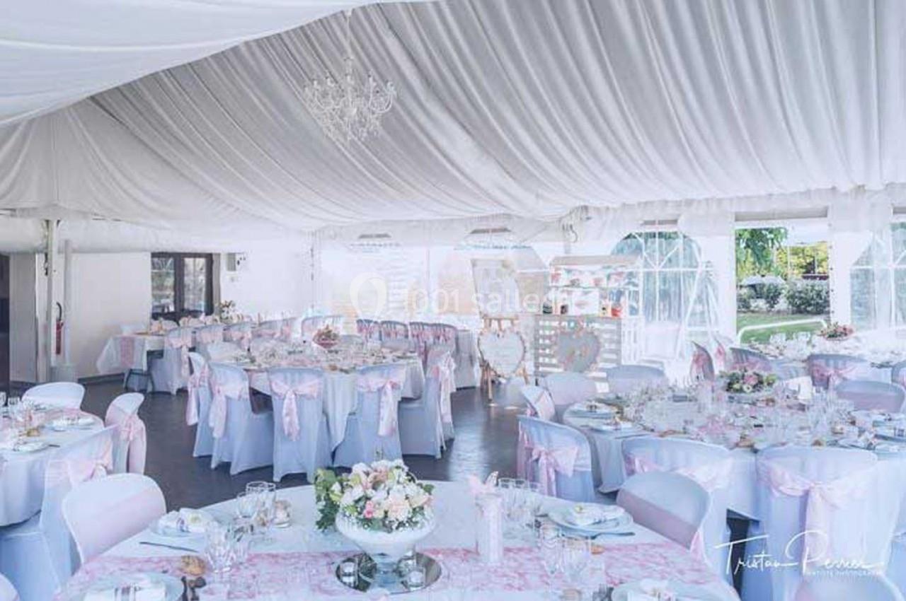 Salle de réception décorée dans des tons pastel avec des tables dressées et des chaises ornées de nœuds roses.