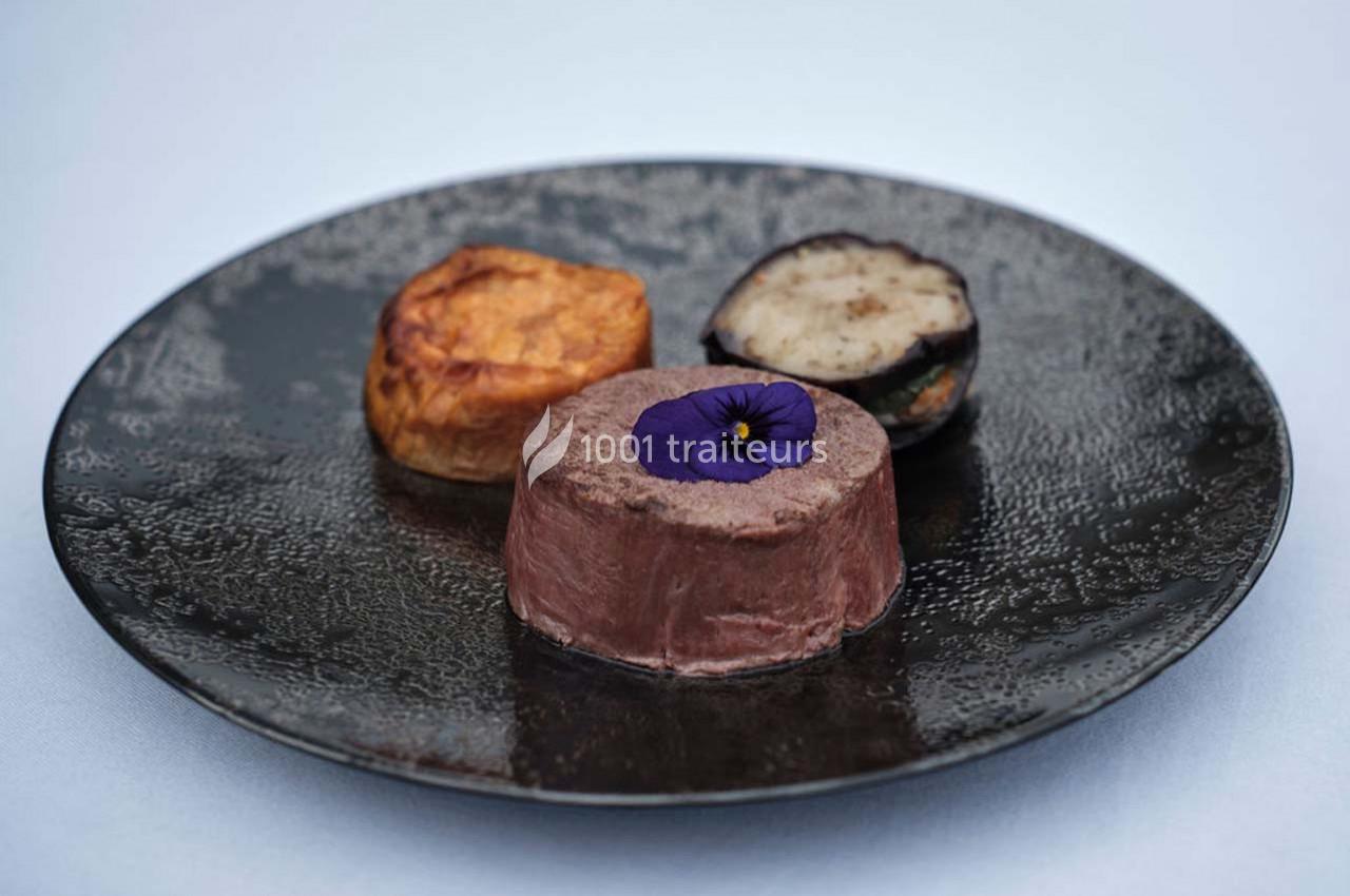 Assiette contenant un médaillon de viande garni d'une fleur comestible, accompagné de légumes rôtis.