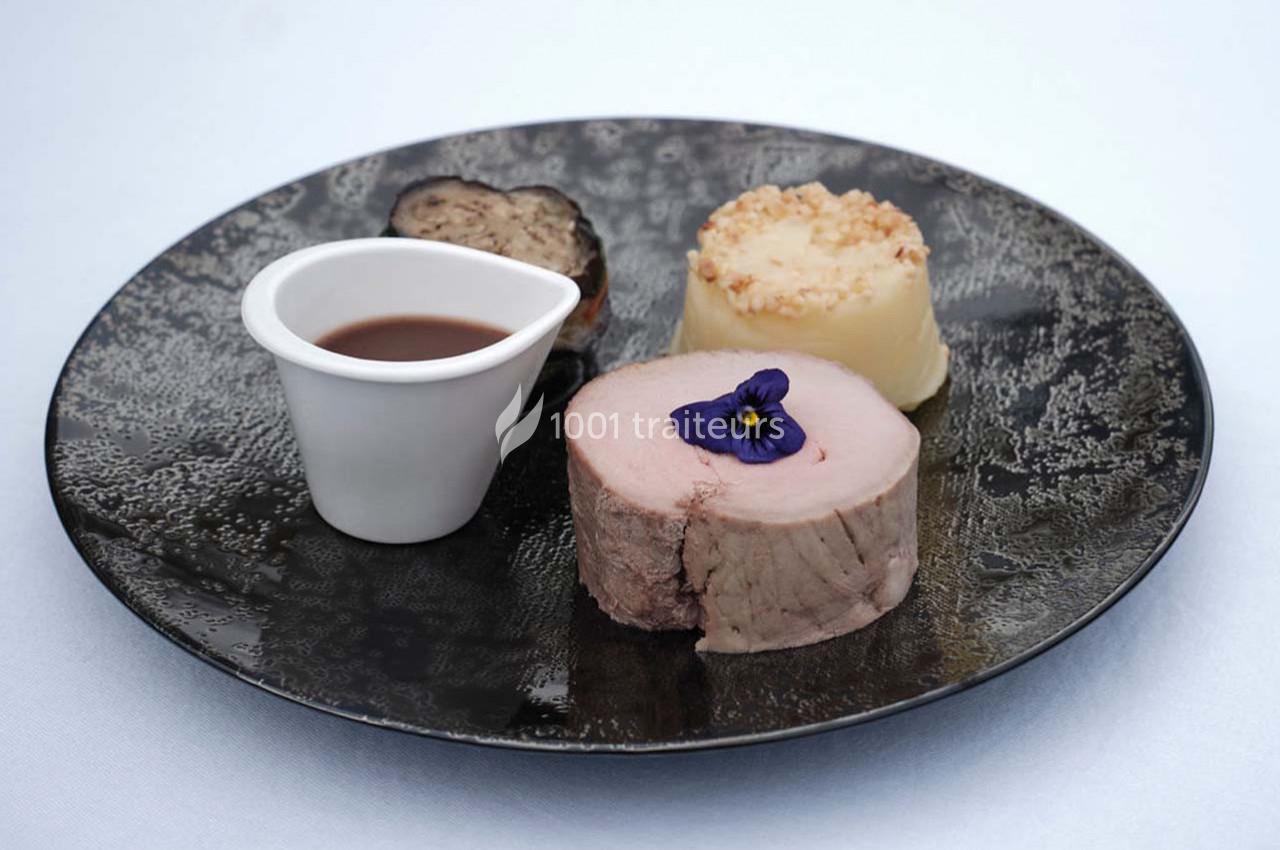 Assiette gastronomique avec viande, purée, truffe, sauce en récipient et fleur comestible en décoration.