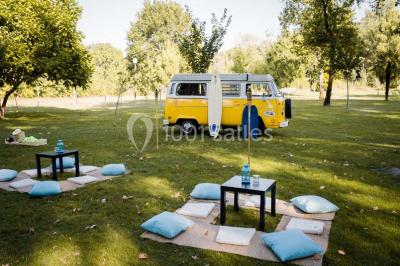 Un kiosque blanc au bord d'un étang avec une fontaine, entouré d'arbres et d'une réception en arrière-plan.