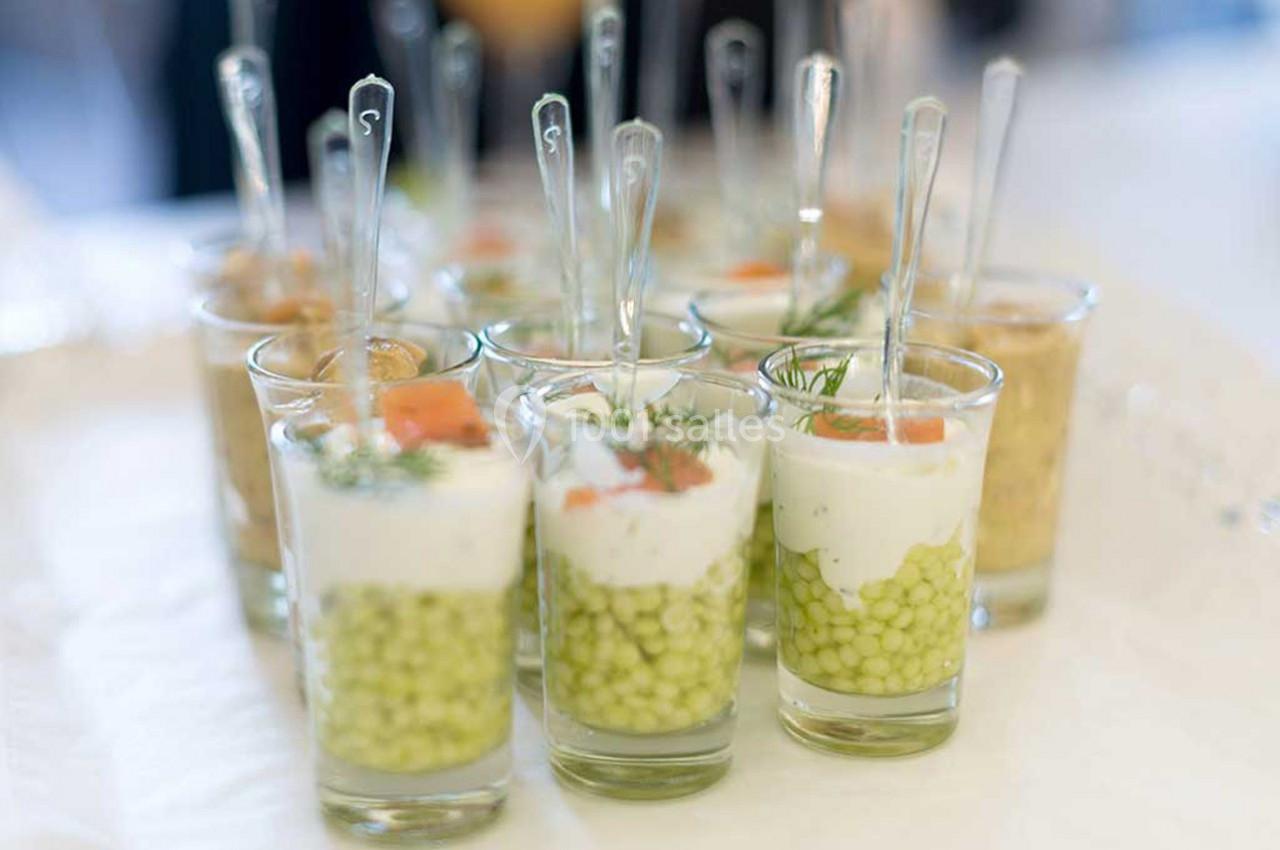 Verrines garnies de petits pois, crème, saumon fumé et aneth, présentées avec des cuillères transparentes.
