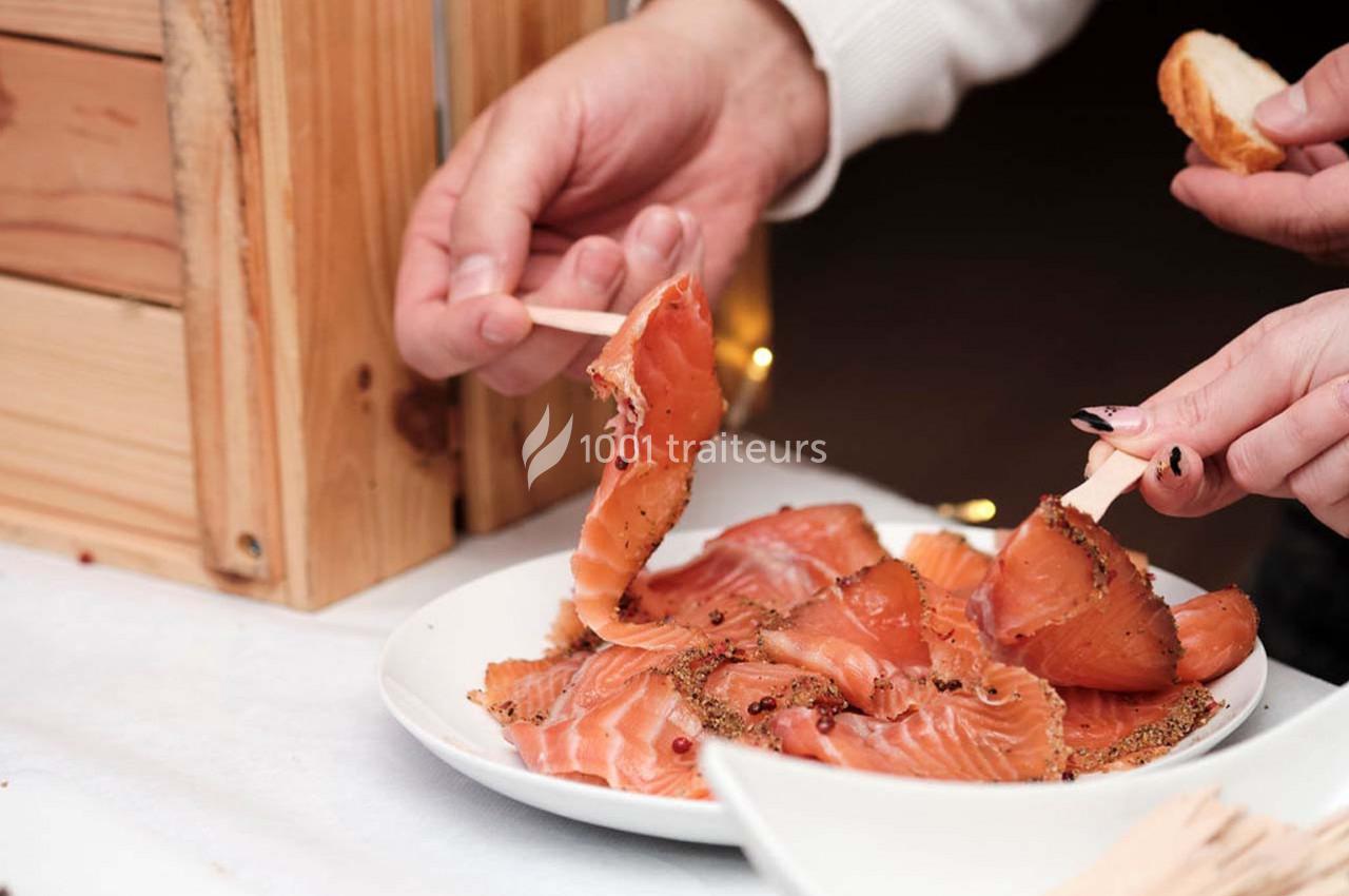 Personne servant des tranches de saumon fumé épicé sur un plateau blanc, avec des pics en bois.