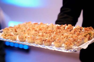 Un kiosque blanc au bord d'un étang avec une fontaine, entouré d'arbres et d'une réception en arrière-plan.