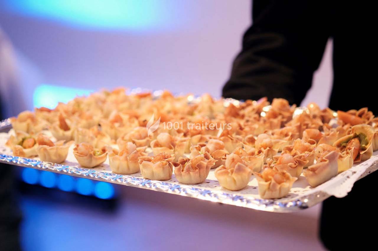 Plateau de bouchées apéritives garnies de charcuterie, présenté par une personne en tenue sombre.