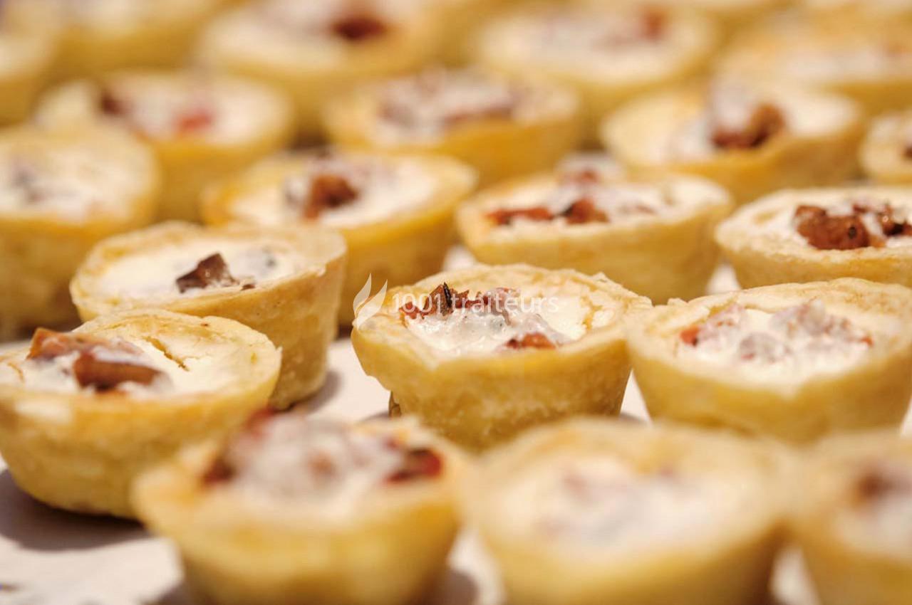 Petites tartelettes salées garnies de fromage et morceaux de viande, disposées sur une surface blanche.