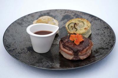 Un kiosque blanc au bord d'un étang avec une fontaine, entouré d'arbres et d'une réception en arrière-plan.