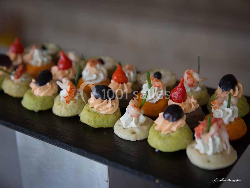 Assortiment de canapés colorés garnis de crème, olives, crevettes et décorations, disposés sur un plateau noir.