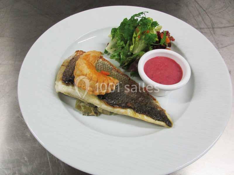 Assiette avec un filet de poisson grillé, une garniture croustillante, une salade verte et une sauce rose en ramequin.