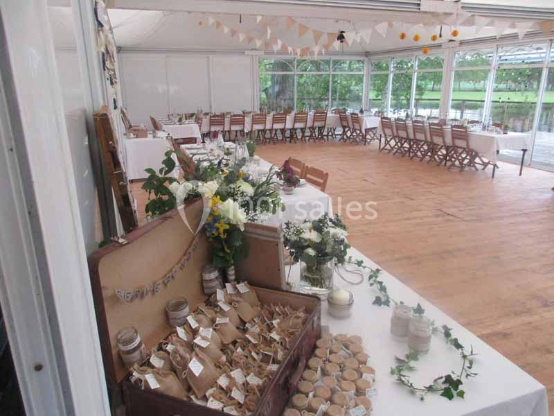Salle de réception lumineuse décorée pour un événement, avec tables dressées et coin cadeaux sur une table.
