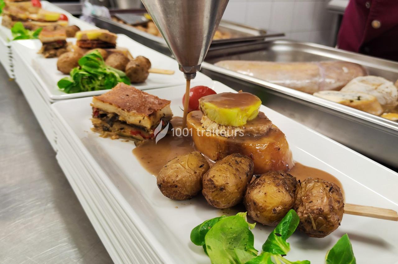 Assiette gastronomique avec viande, pommes de terre rôties, légumes et sauce servie dans une cuisine professionnelle.