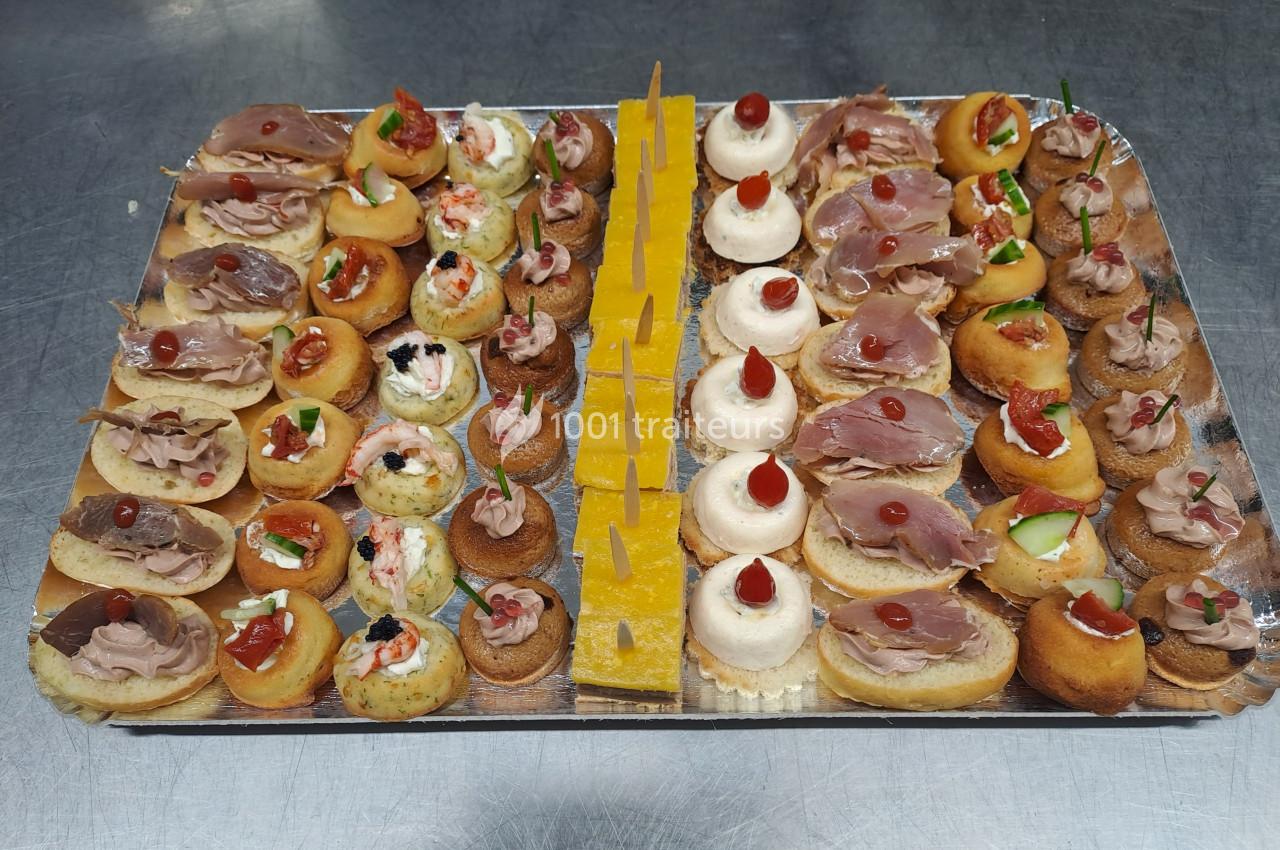 Plateau de canapés variés avec des garnitures salées, disposés de manière symétrique sur une surface métallique.
