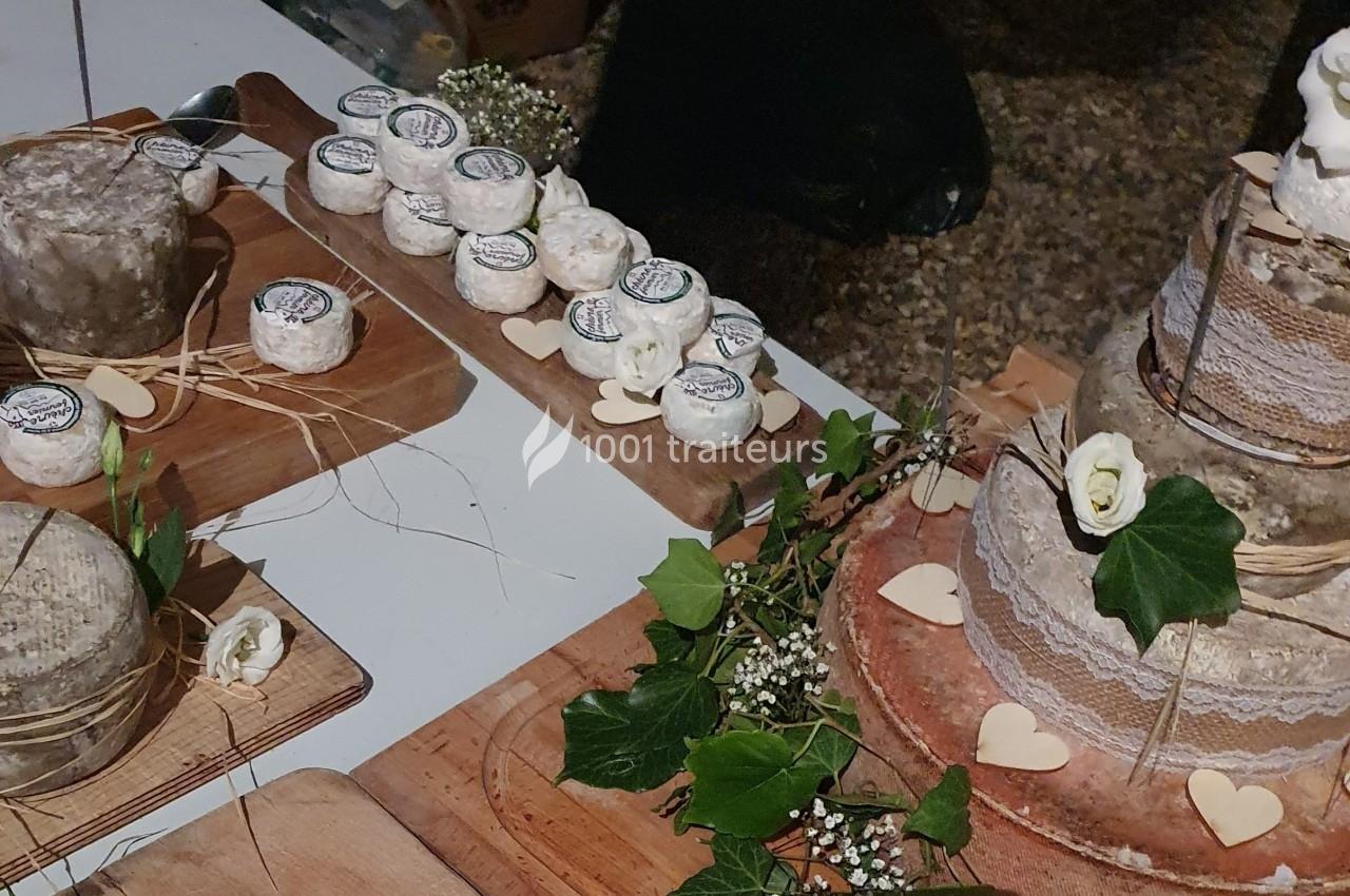 Plateaux de fromages variés, dont un en forme de pièce montée décorée de feuillage et de fleurs blanches.