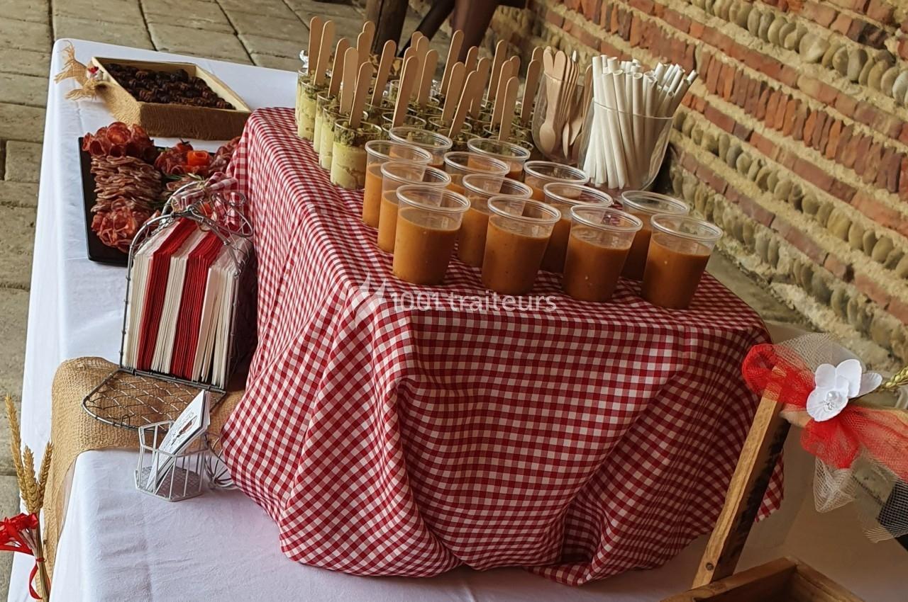 Buffet avec verrines, brochettes et couverts en bois sur une nappe à carreaux rouges et blancs.