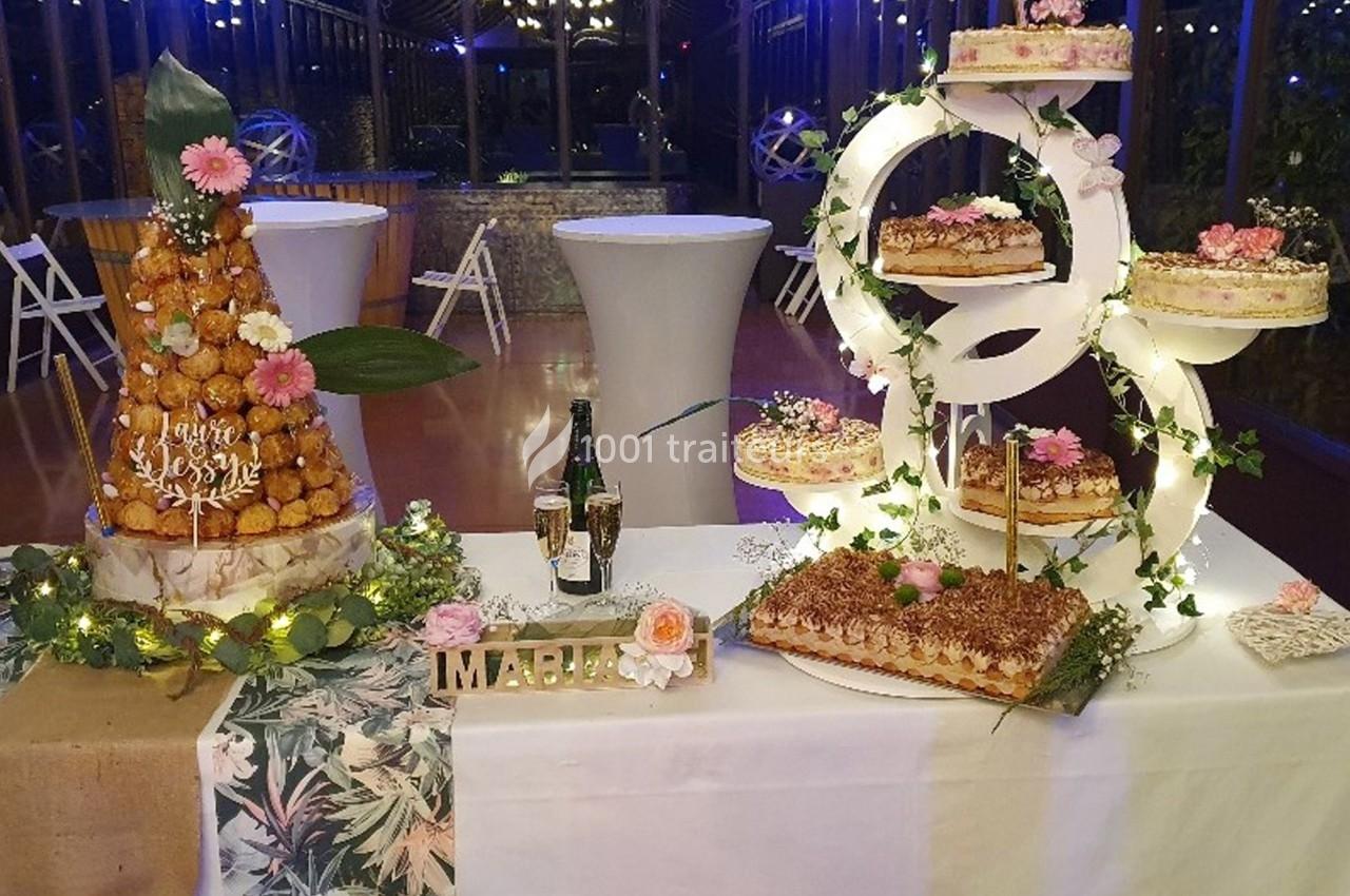 Table décorée pour un événement avec pièces montées, gâteaux, champagne et ornements floraux dans une salle éclairée.