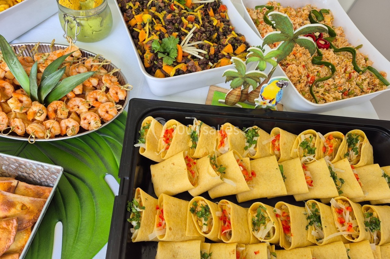 Buffet coloré avec wraps garnis, brochettes de poulet, salade de riz et plat de légumes noirs et orange.