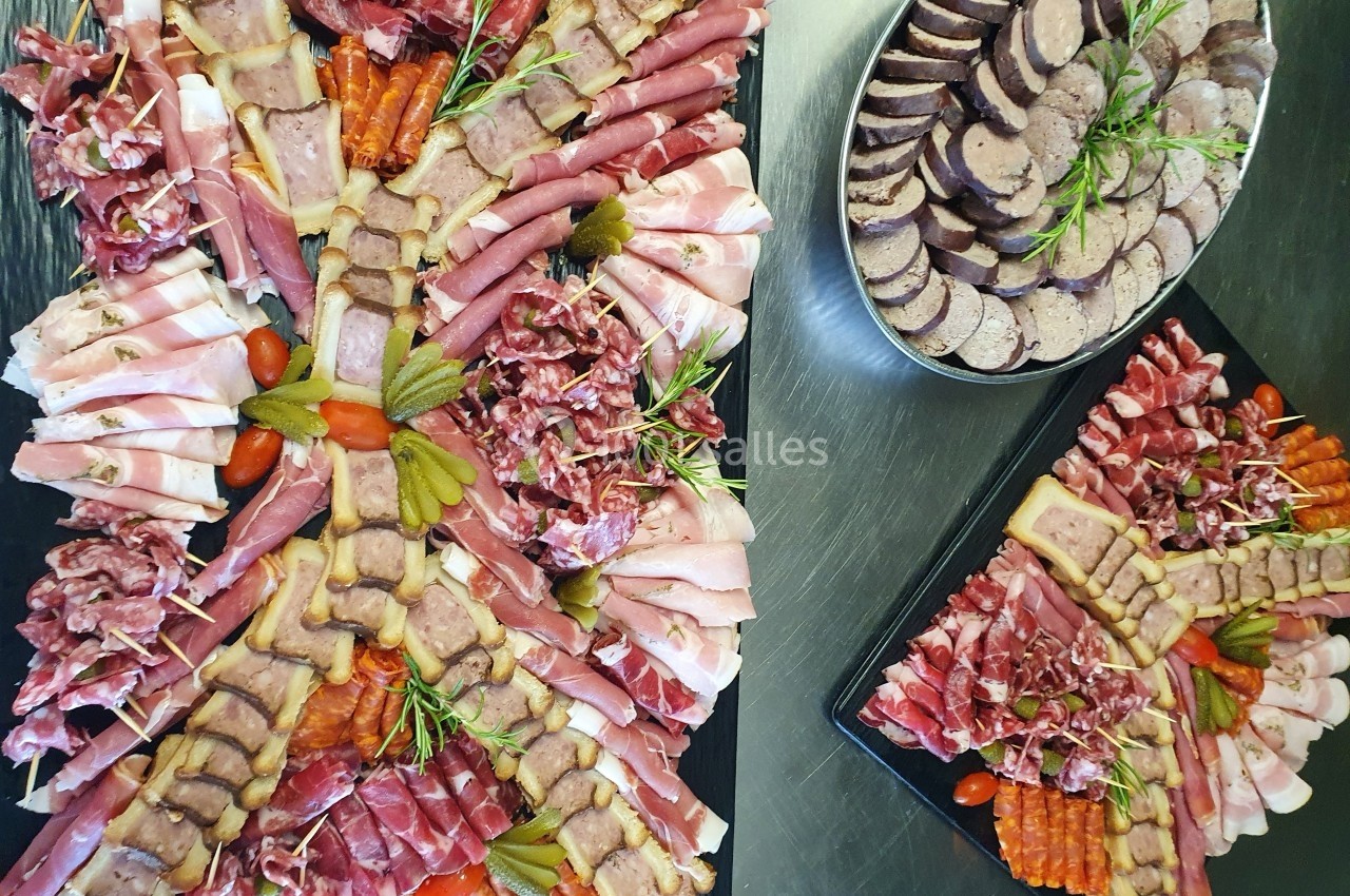 Plateaux de charcuterie variée avec jambon, saucisson, cornichons et terrine, présentés sur une table.