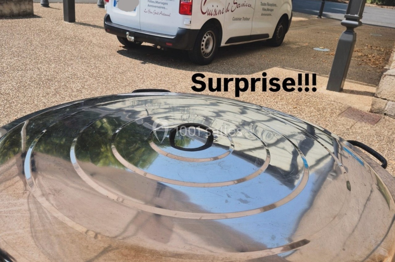 Vue rapprochée d'un couvercle métallique réfléchissant, avec une camionnette de traiteur stationnée en arrière-plan.