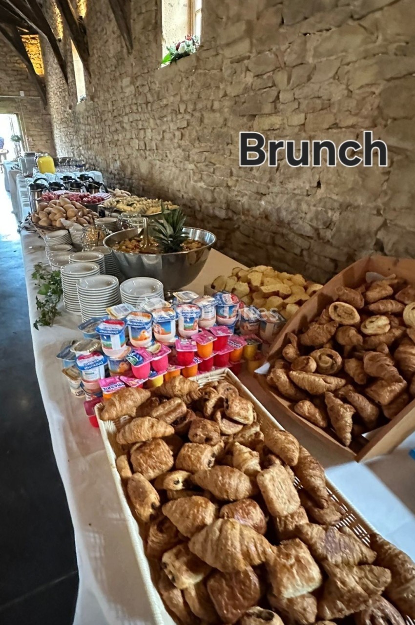 Buffet de brunch avec viennoiseries, yaourts, fruits et autres plats disposés sur une longue table dans une salle en pierre.
