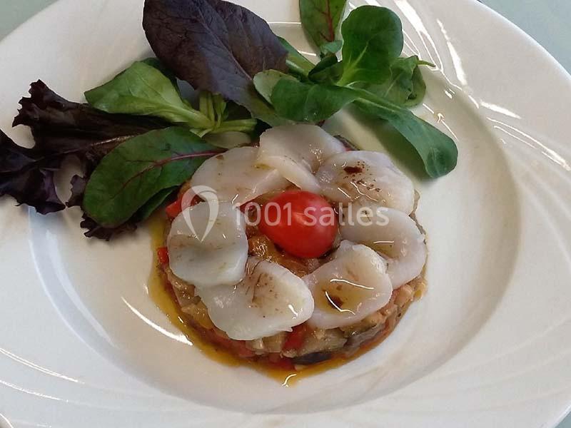 Tartare de légumes colorés surmonté de fines tranches de Saint-Jacques, décoré de jeunes pousses et d'un tomate cerise.