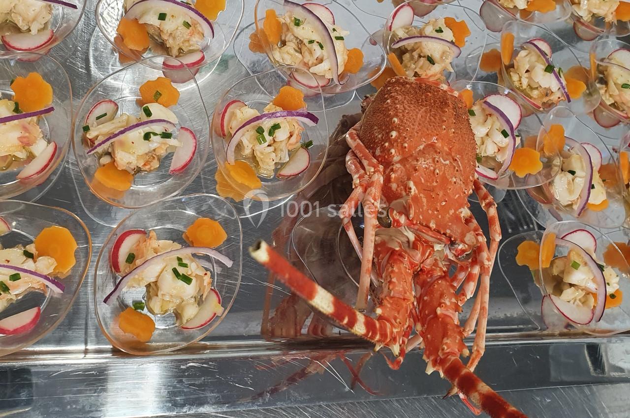Plateau de verrines de fruits de mer garnies de légumes, avec un homard entier en présentation au centre.