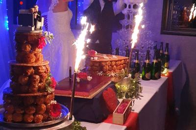 Tour de choux décorée avec des fleurs et des étincelles, entourée de desserts sur une table de réception.