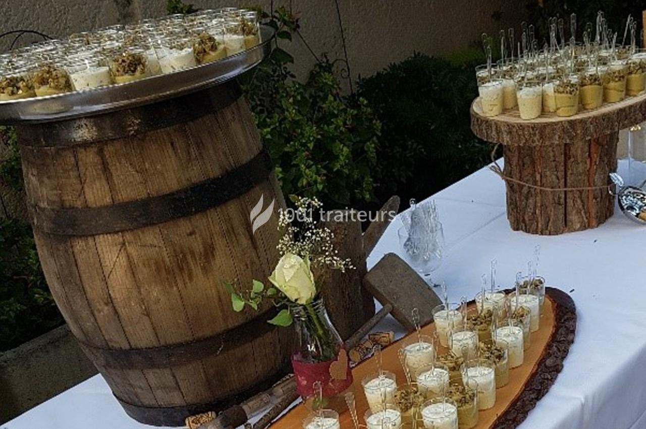 Buffet en extérieur avec verrines disposées sur une table blanche, un tonneau en bois et des rondins décoratifs.