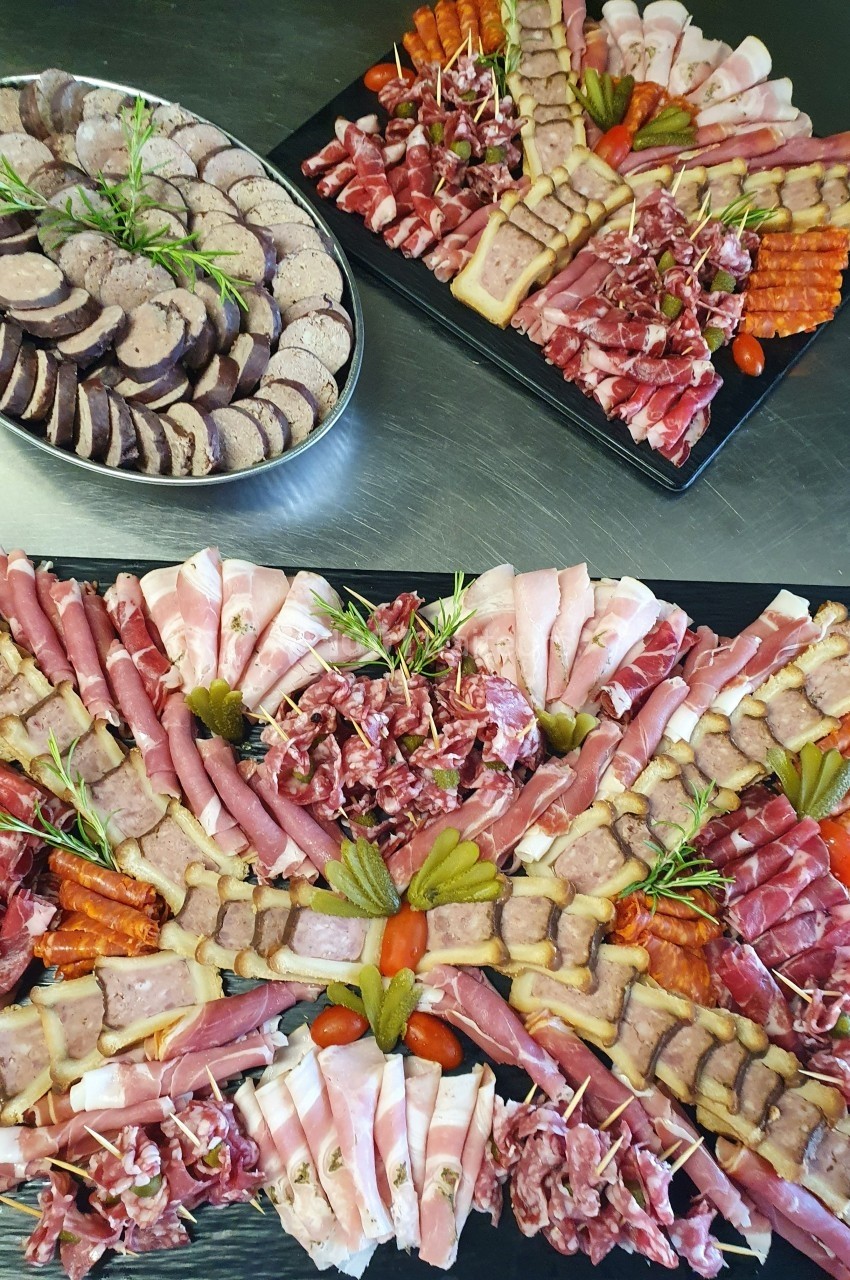 Plateaux de charcuterie variée avec jambon, saucisson, pâté et cornichons, décorés de brins de romarin.