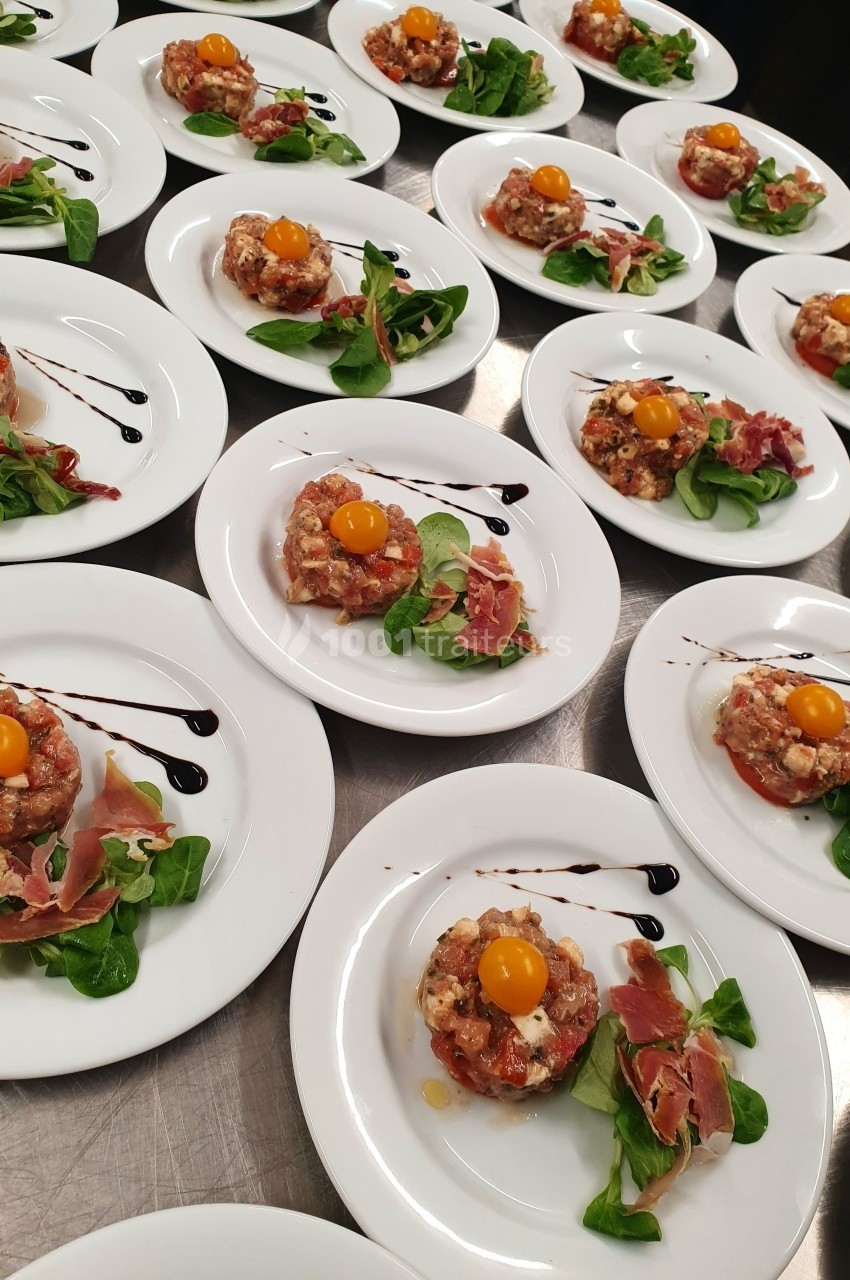 Assiettes dressées avec tartares de viande, jaunes d'œufs, feuilles de salade, jambon cru et filet de sauce balsamique.