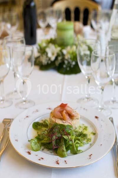 Assiette dressée avec une entrée composée de saumon fumé, salade verte et herbes, sur une table élégamment décorée.