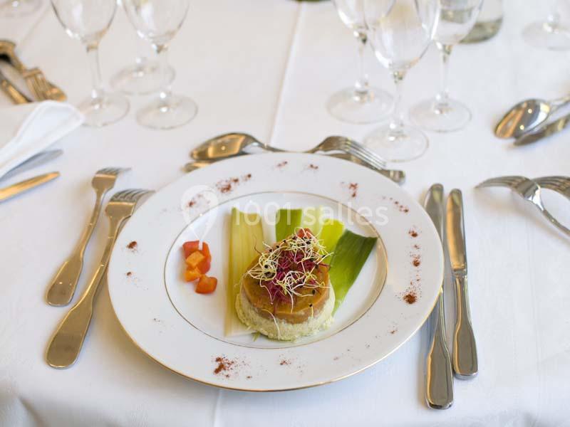 Assiette gastronomique avec une entrée composée de légumes, d'une purée et de germes, présentée sur une table dressée.
