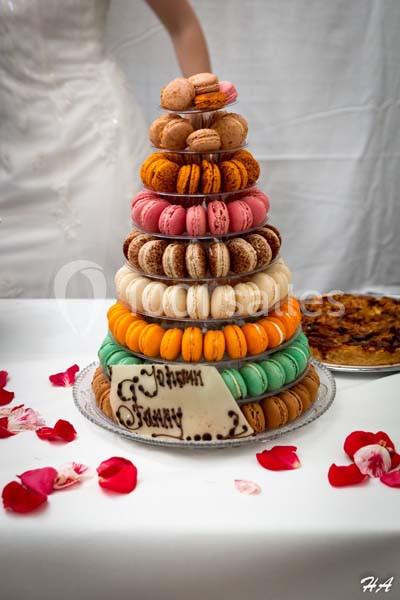 Tour de macarons colorés surmontée de petits gâteaux, avec une plaque en chocolat et des pétales de rose autour.