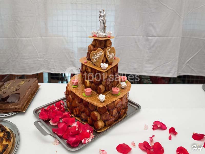 Pièce montée de choux décorée de roses en sucre, de cœurs en biscuit et d'une figurine de mariage au sommet.