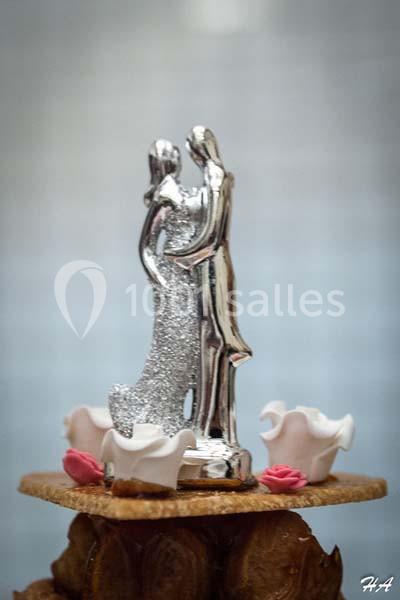 Figurine argentée représentant un couple enlacé, posée sur une pièce montée décorée de fleurs en sucre.