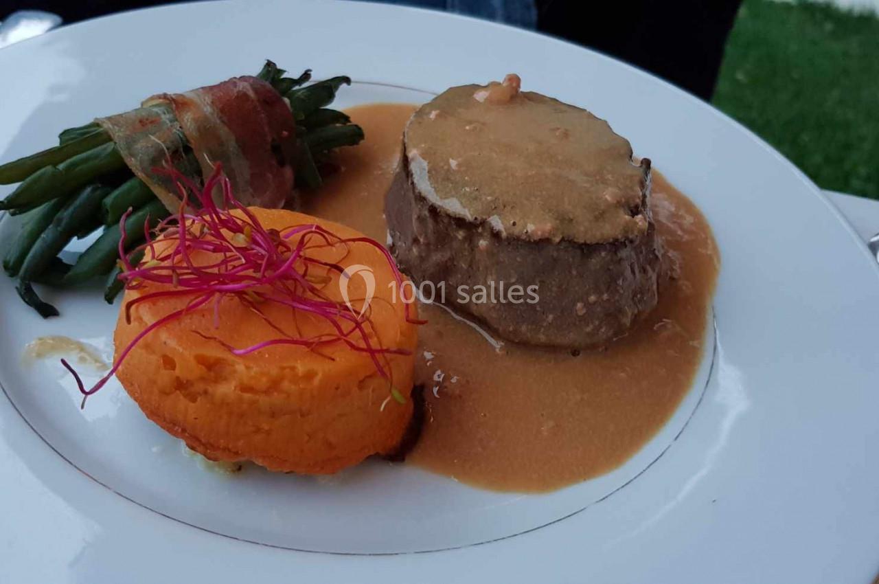 Assiette contenant un filet de viande en sauce, une purée de patate douce et des haricots verts enroulés de lard.