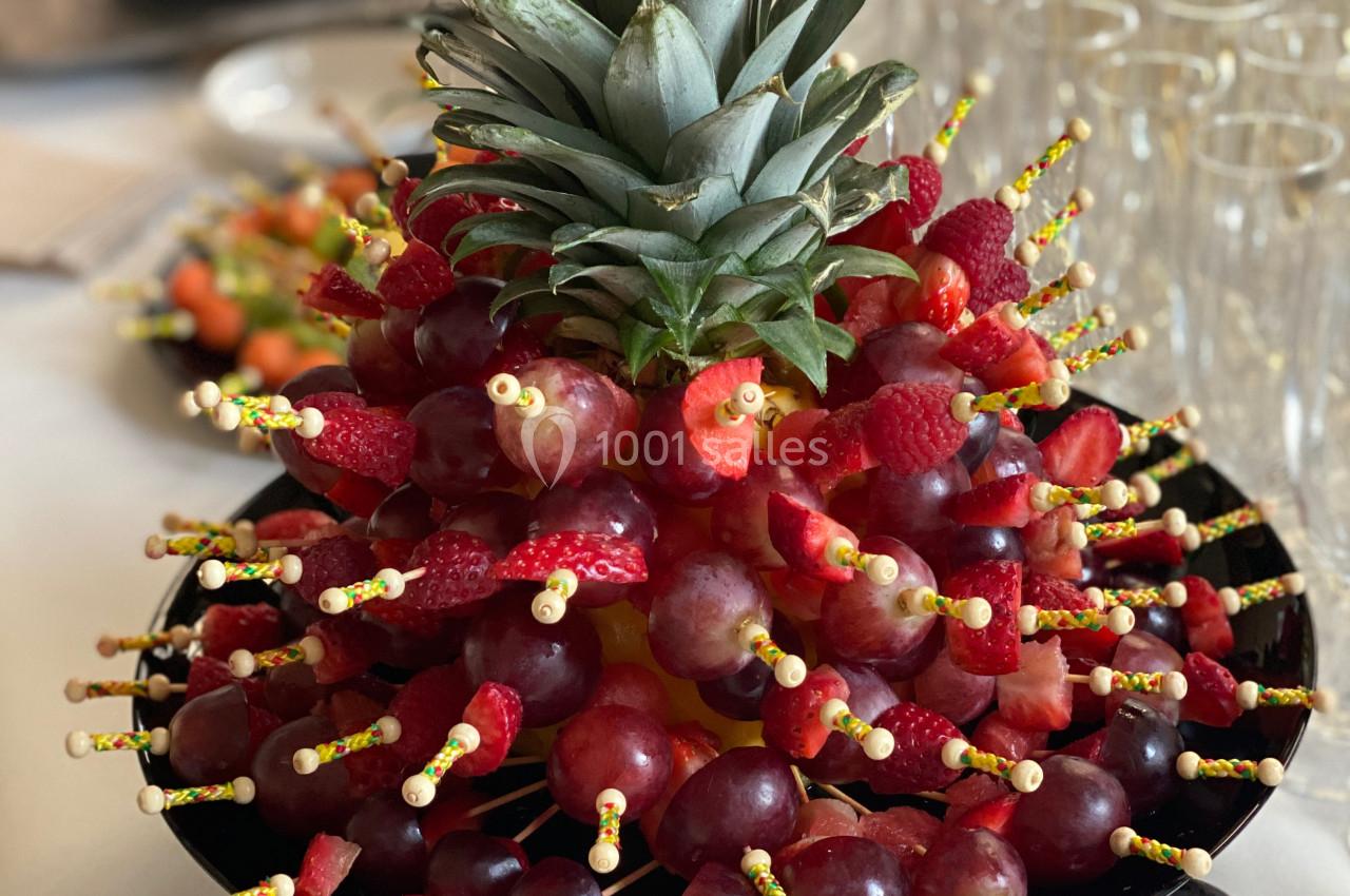 Brochettes de fruits variés, principalement raisins et fraises, disposées autour d'un ananas sur un plateau.