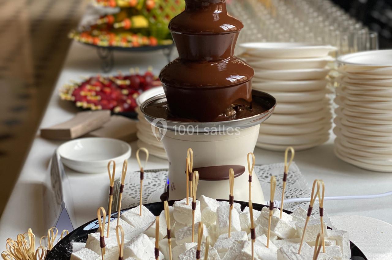 Fontaine de chocolat entourée de brochettes de guimauves et d'autres desserts disposés sur une table de réception.