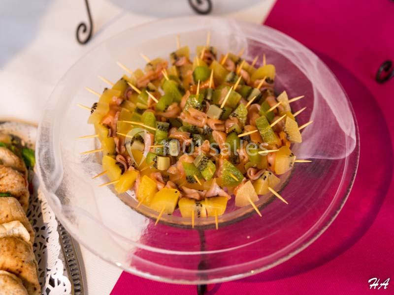 Brochettes apéritives composées de fruits et de morceaux de saumon, présentées sur une assiette en verre.