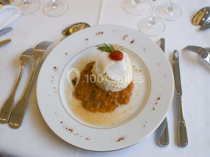 Assiette dressée avec un médaillon de poisson sur un lit de sauce tomate, accompagnée de couverts sur une nappe blanche.