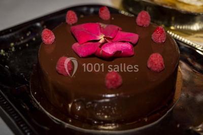 Gâteau au chocolat décoré de framboises et d'une fleur rose, présenté sur un plateau sombre.