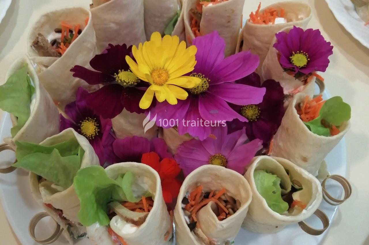 Plateau de wraps garnis de légumes frais, décoré de fleurs comestibles colorées au centre.