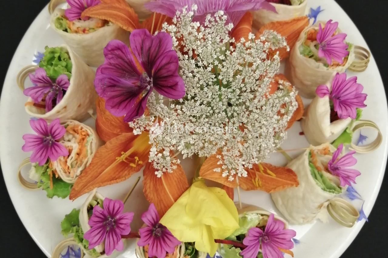 Assiette garnie de wraps colorés entourés de fleurs comestibles et décoratives.