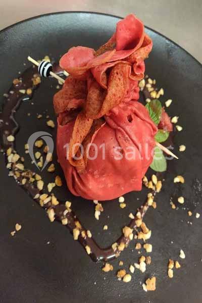 Crêpe rouge garnie et nouée, servie sur une assiette noire avec sauce chocolat et éclats de noisettes.