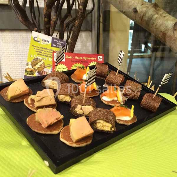 Plateau de mini-bouchées variées comprenant foie gras, saumon fumé et autres garnitures, présenté sur une nappe verte.